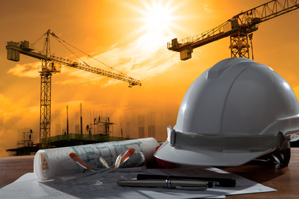safety helmet and architect pland on wood table with sunset scene and building construction